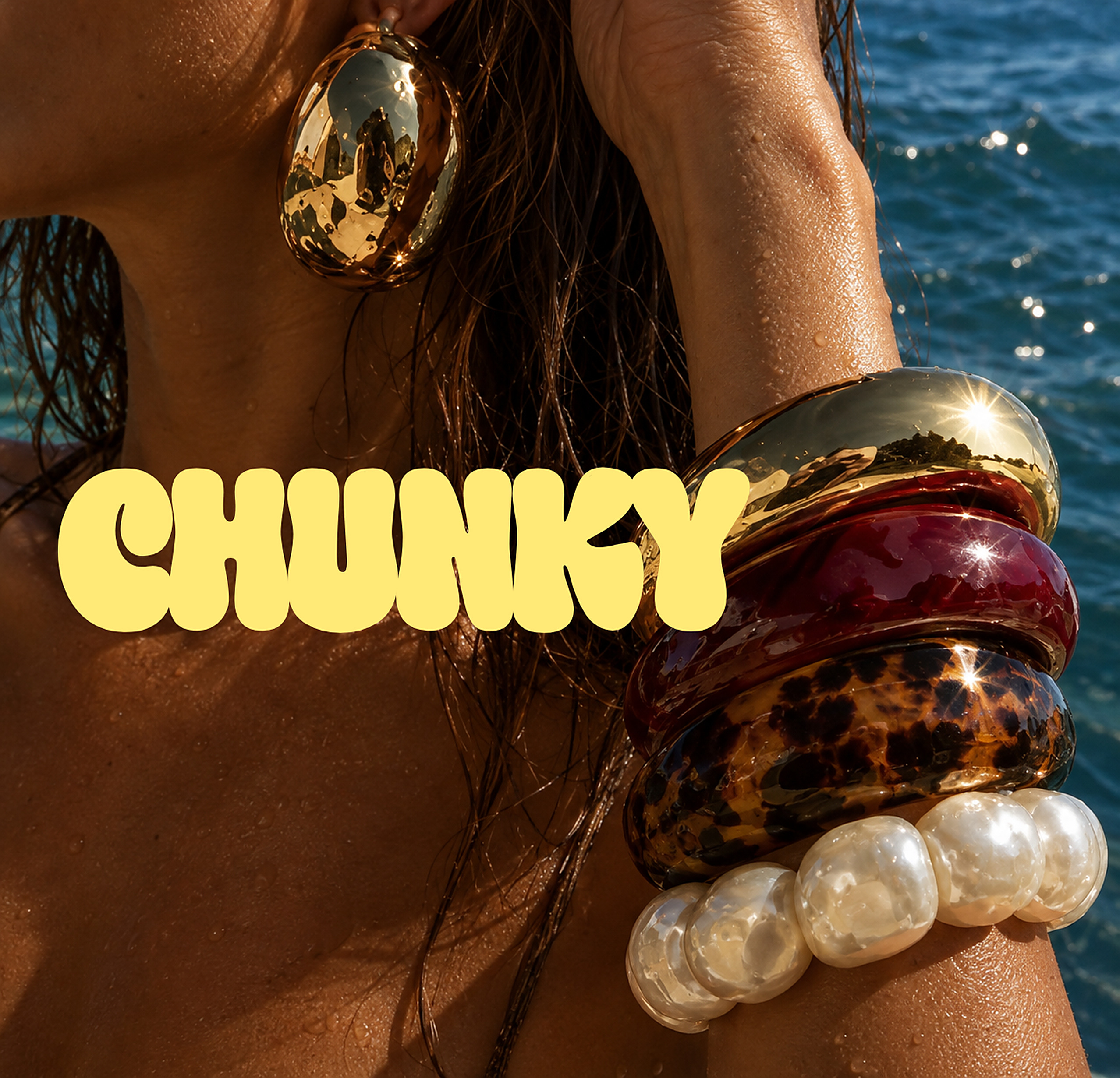 CHUNKY-loggan över en solbränd arm med staplade bangles i guld, vinrött, sköldpadd och pärlor framför havet